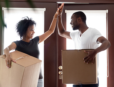 IMAGE: Couple holding moving boxes and high-fiving inside doorway