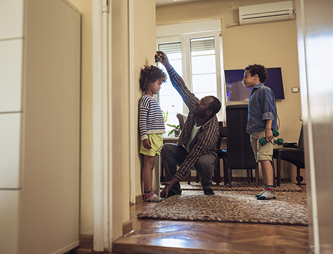 IMAGE: a father measuring the height of his children.