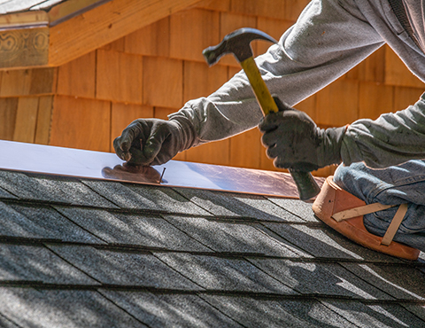 IMAGE: a roofer nailing shingles on a roof